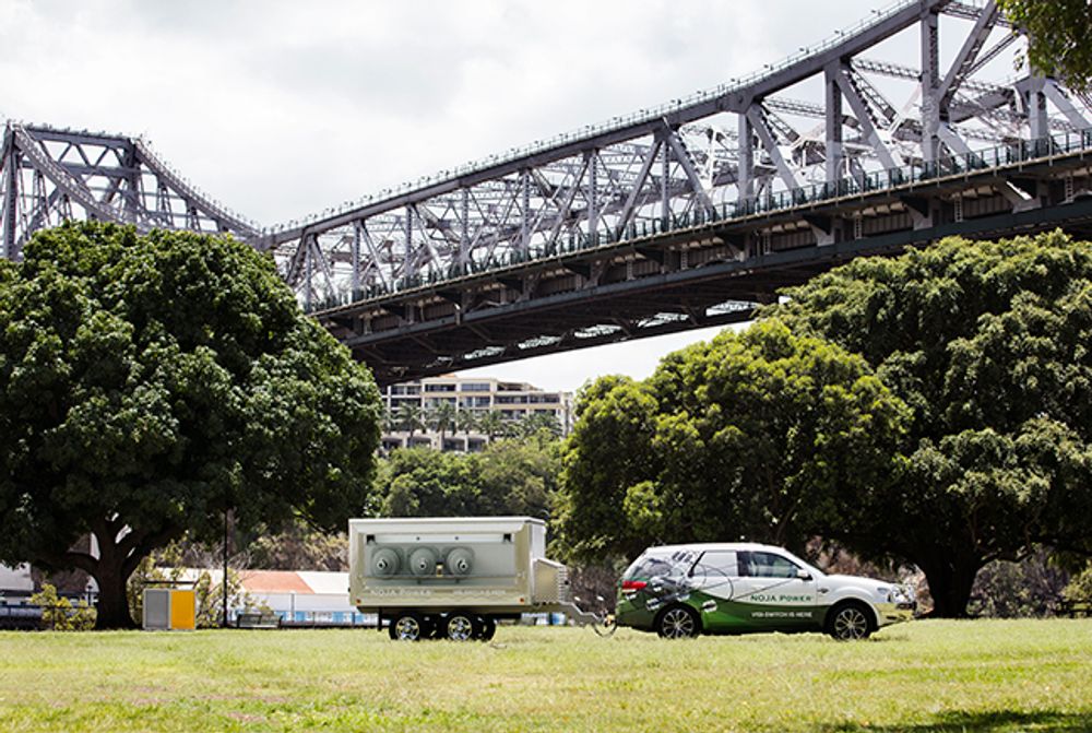 NOJA Power Trailer parked on the grass in front of trees and with Brisbane Story Bridge in the background 