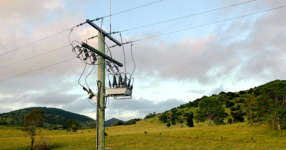 Pole mounted NOJA Power Installation in the centre left foreground of the image, with Australian mountains and blue and grey skies in the background 