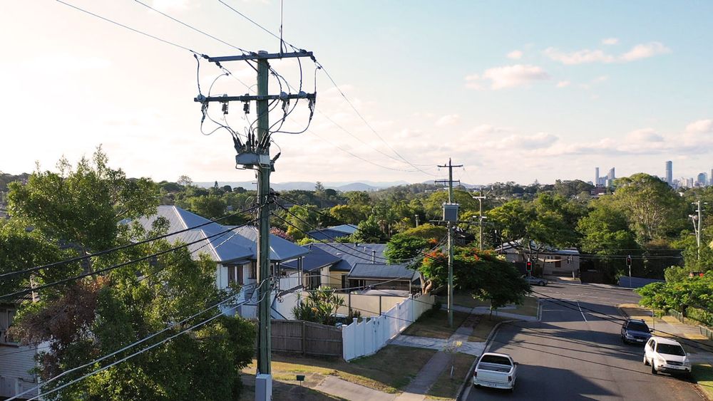 NOJA Power Recloser installation in the suburbs of Brisbane, with a grey and white house, surrounding streets and cars in the background