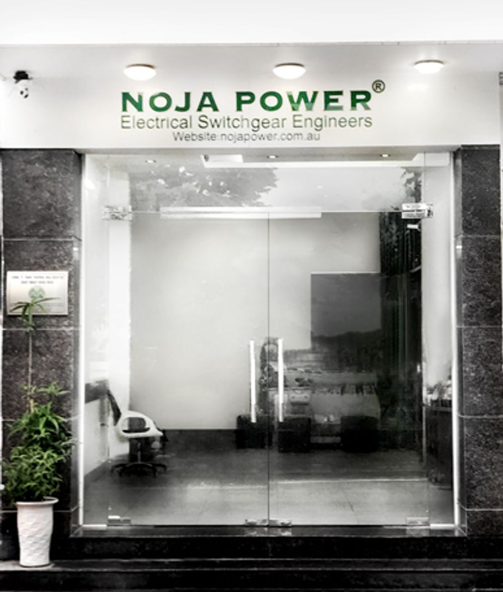 Image of office building glass doors with NOJA Power branding over the door. Next to door is a plant.