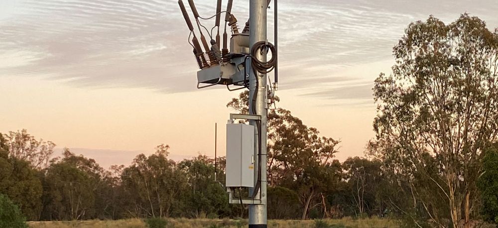 Pole mounted NOJA Power OSM Recloser and RC10 with the sun setting on the Australian landscape in the backgroun