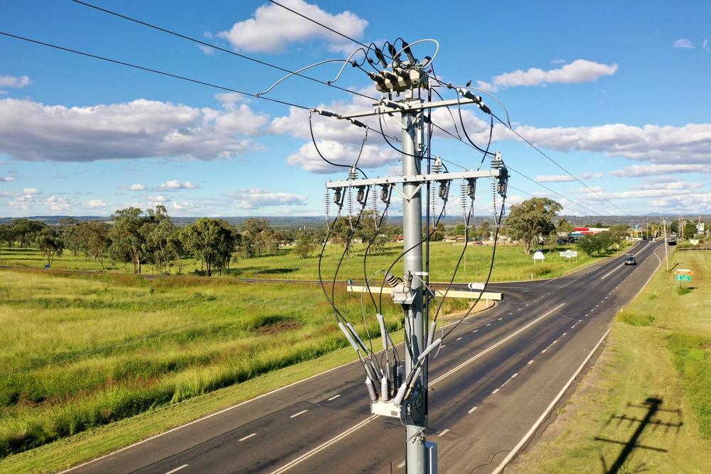 Pole mounted NOJA Power Installation in Regional Australia above a road, surrounded by grass with blue skies and scattered clouds