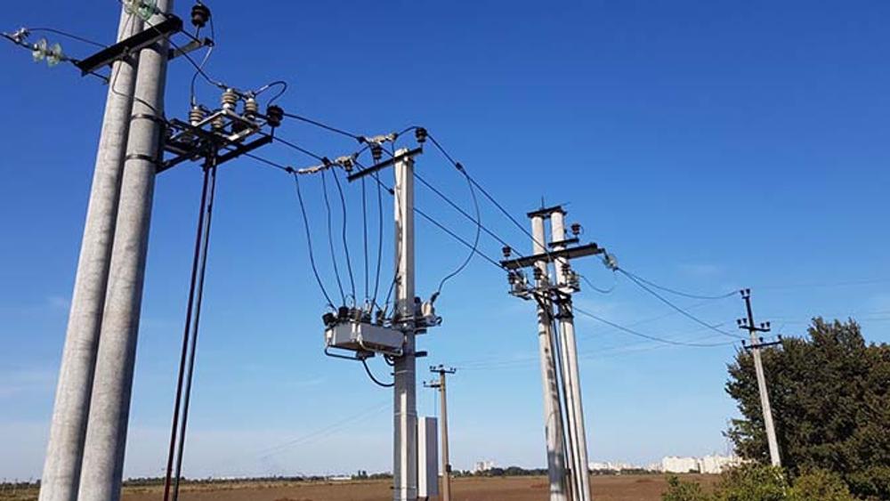 Four powerlines in front of dirt field, with a NOJA Power OSM Recloser in the center of the pole