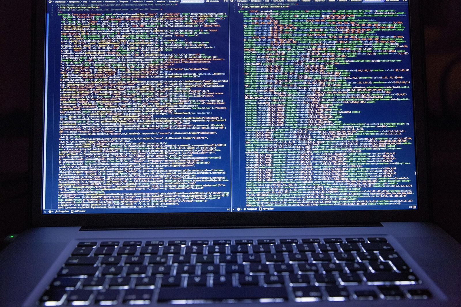 Laptop screen showing two side-by-side panes of colorful source code in a code editor, above a dark keyboard