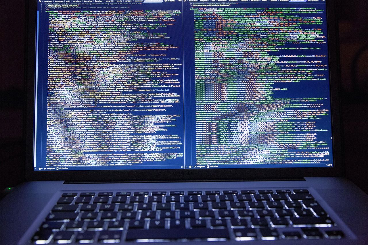Laptop screen showing two side-by-side panes of colorful source code in a code editor, above a dark keyboard