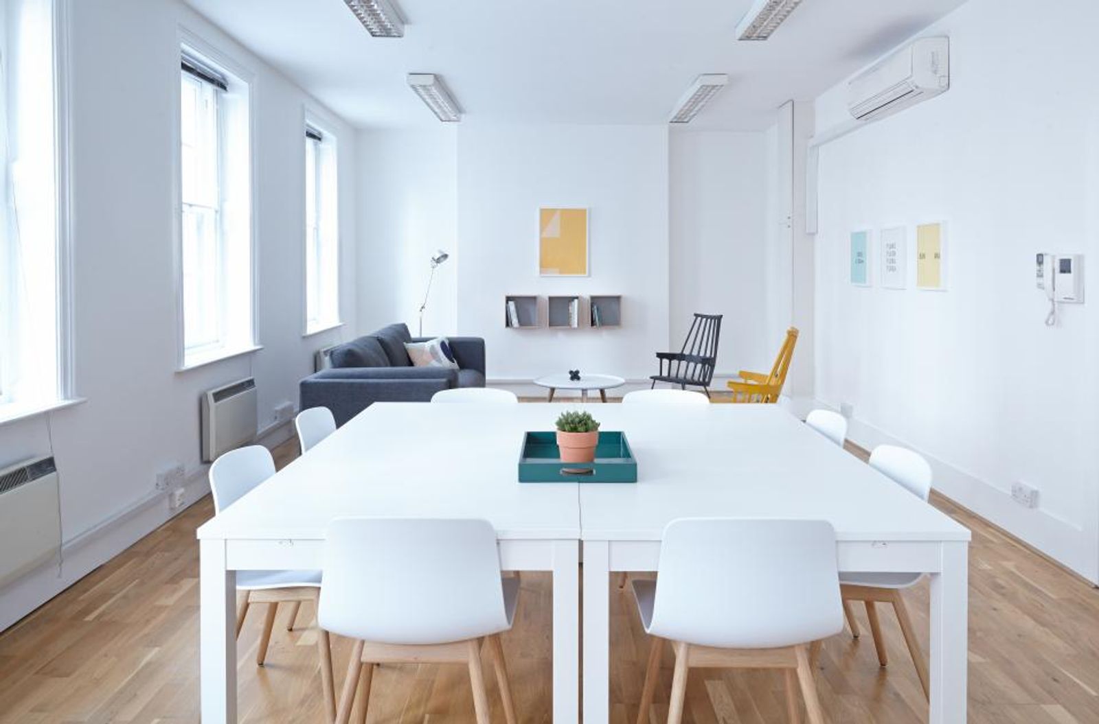 Bright office room with a white conference table, white chairs, a teal tray with a plant, and a gray sofa