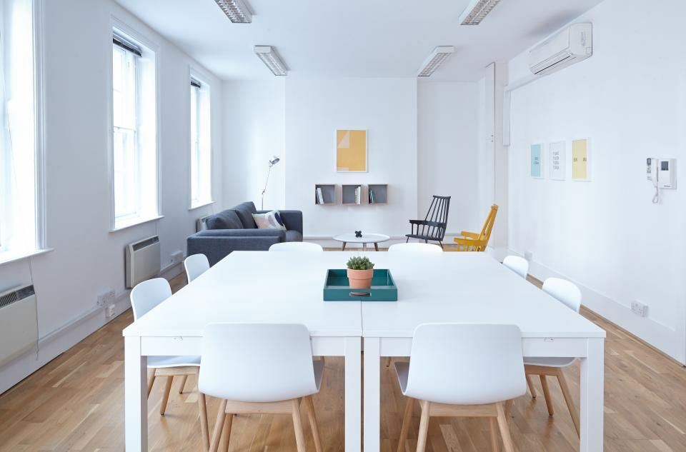 Bright office room with a white conference table, white chairs, a teal tray with a plant, and a gray sofa
