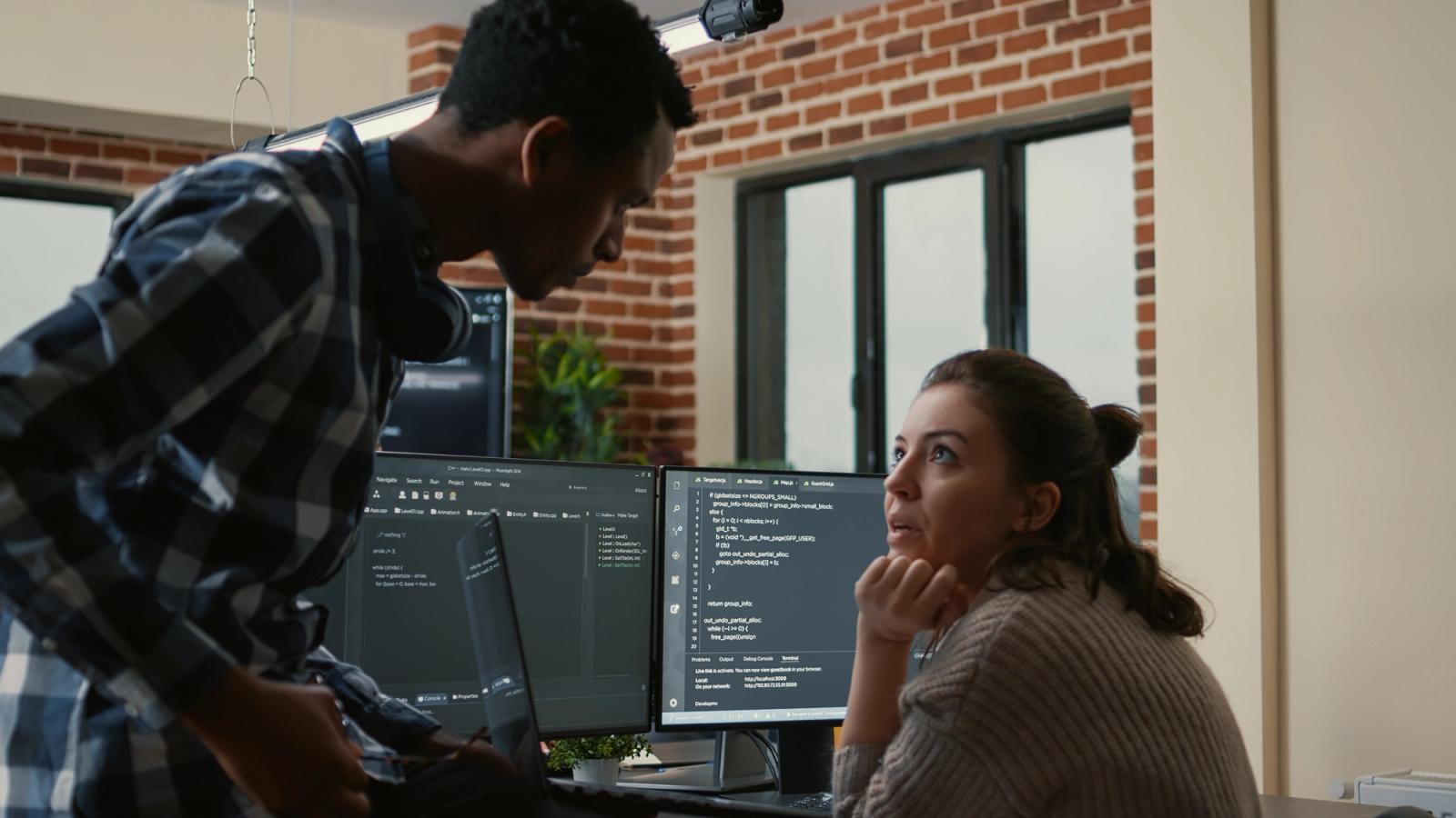 A junior developer showing a senior developer test code on a laptop at a desk