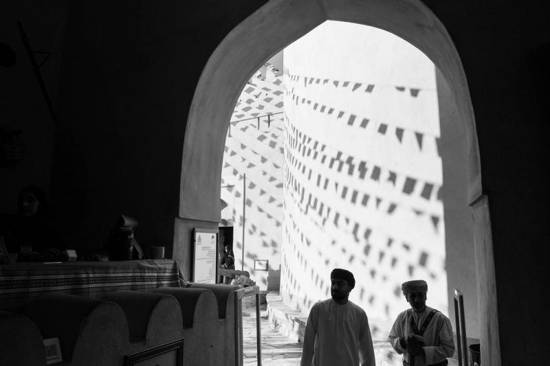 Two men in the entrance of Nizwa fort, surrounded by the shadows of flags.