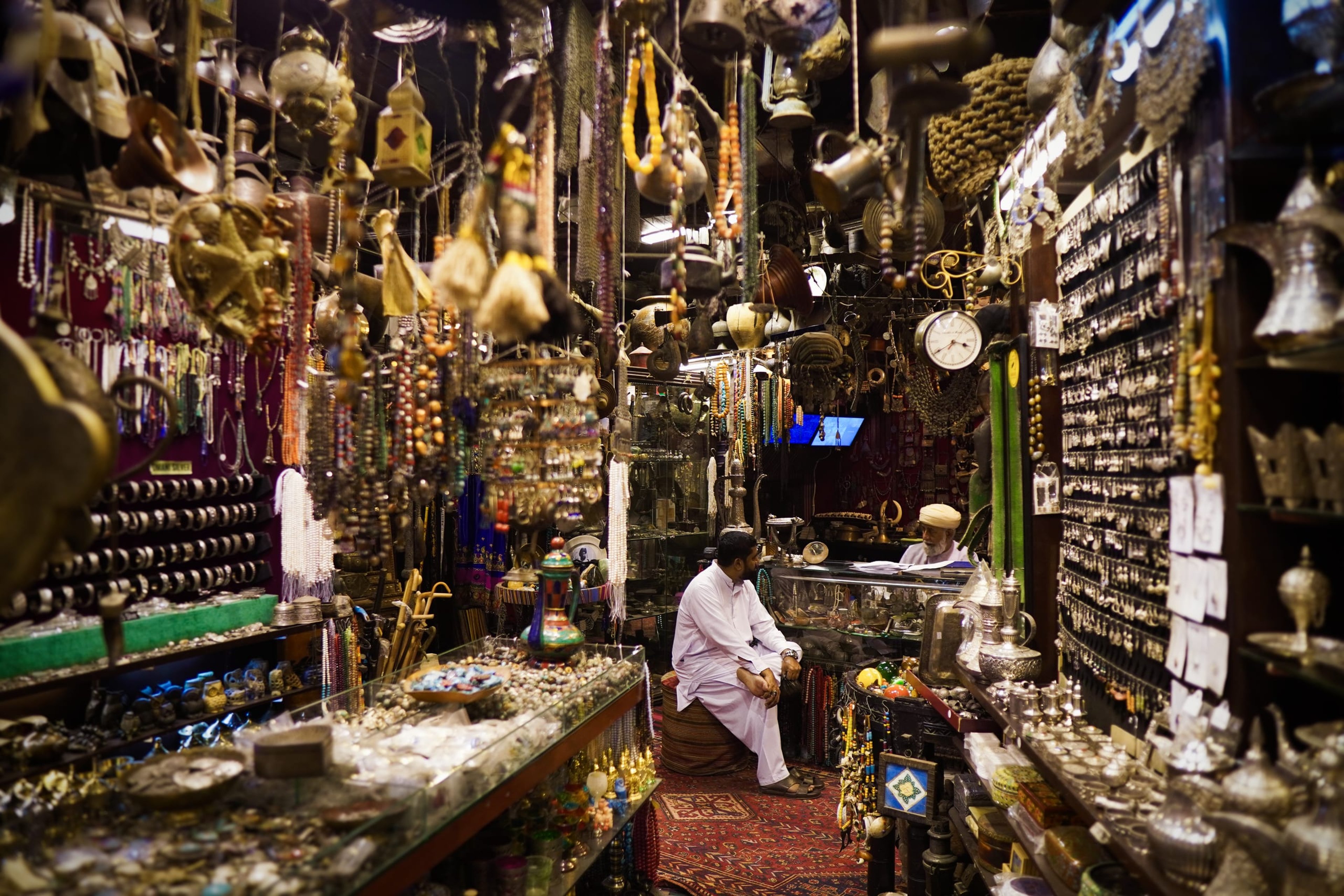 Two men in conversation, surrounded by trinkets of silver and gold.