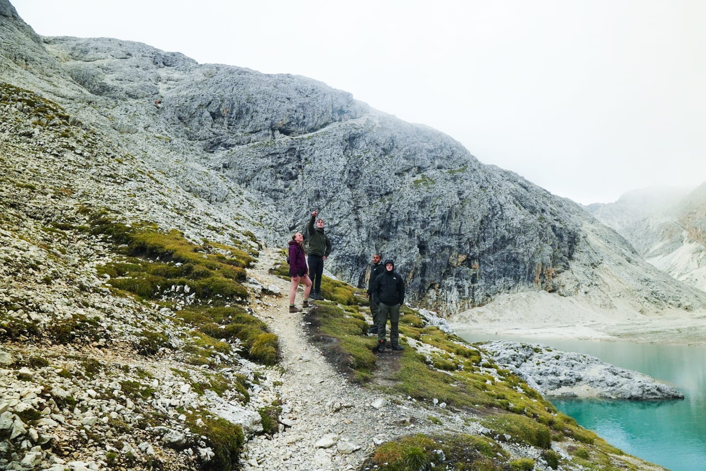 Four hikers on a mossy hill beside a turquoise lake