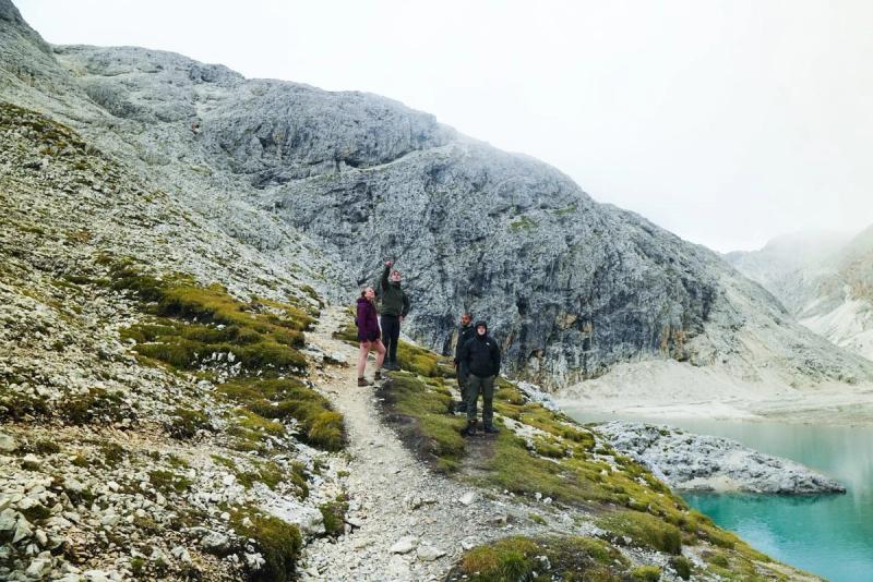 Four hikers on a mossy hill beside a turquoise lake