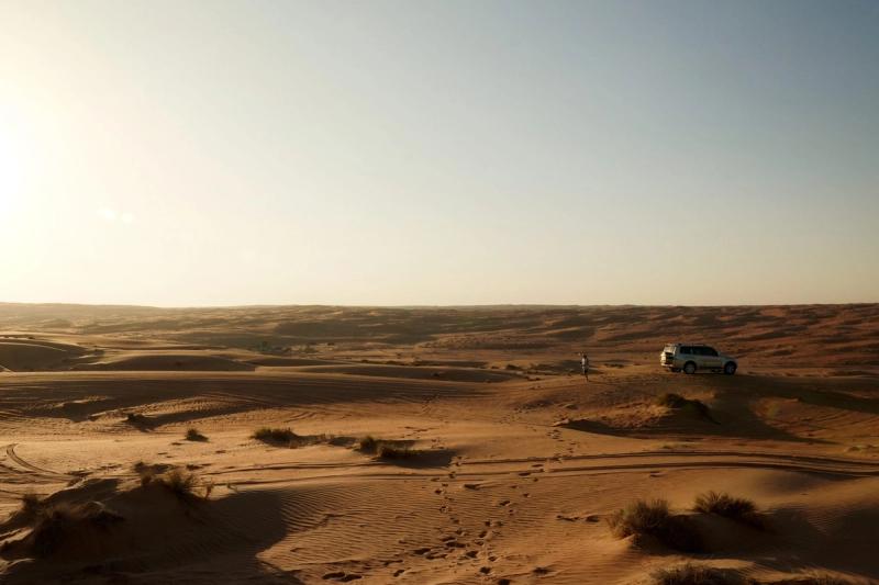 Footsteps in sand, leading to a car surrounded by dunes of desert