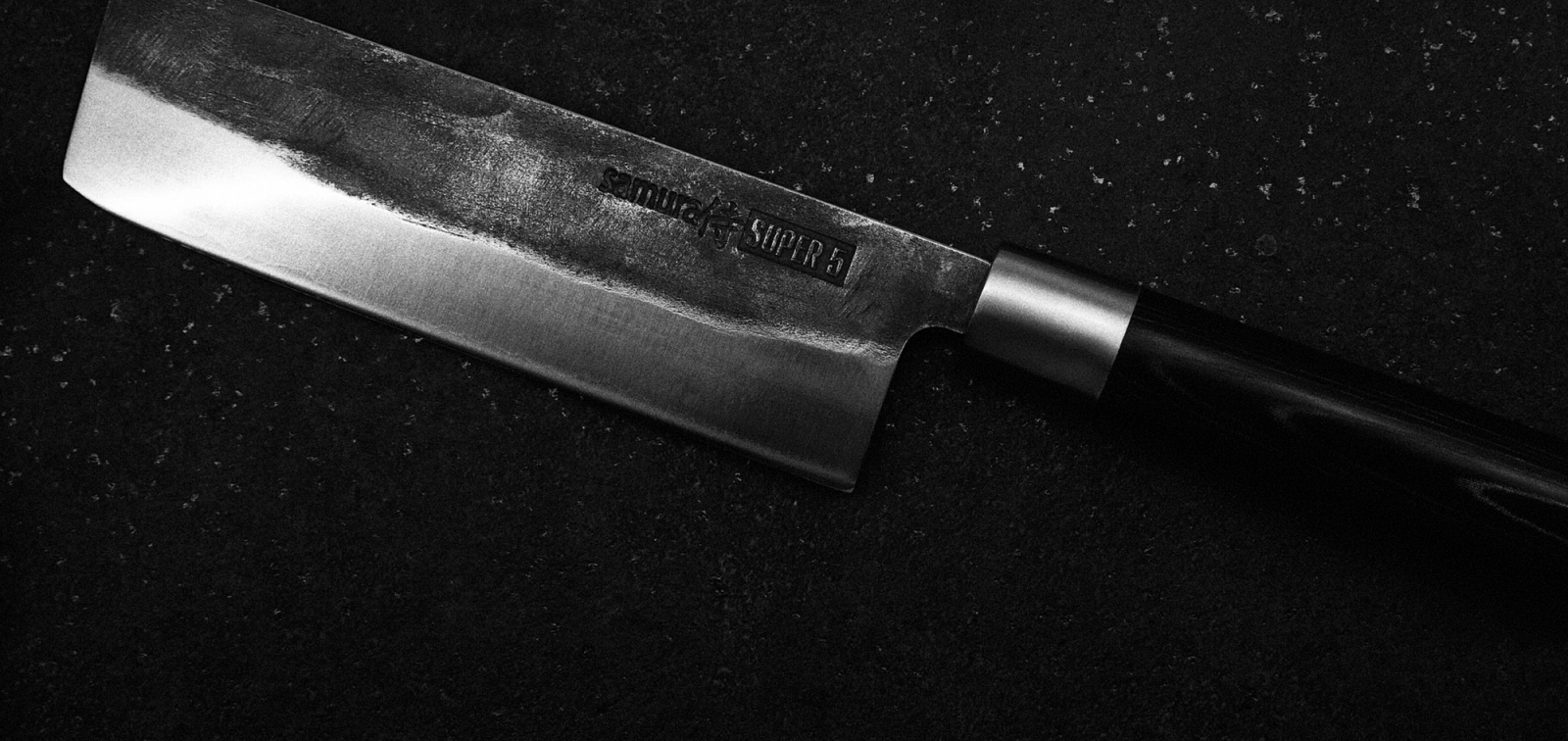 A chef's knife resting on a dark surface