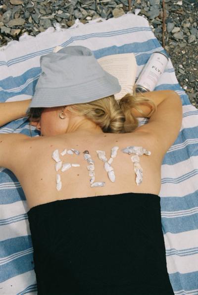 Lady sleeping on the beach with a can of flyt with flyt written on her back with shells