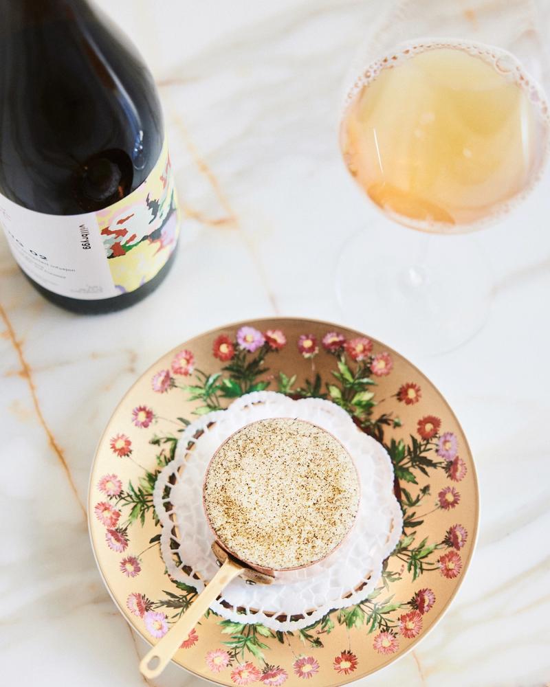 Villbrygg ENG served in a wine glass alongside a decorative dessert and bottle, on a marble table with a floral plate.