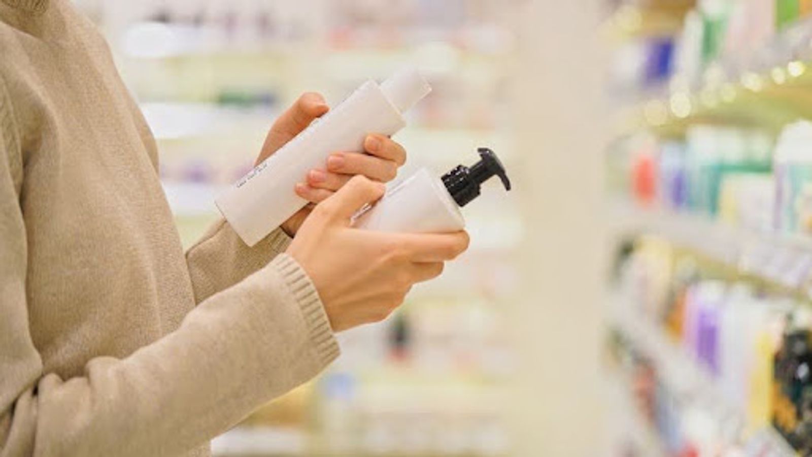 person looking at a bottle and reading ingredients on the back of it with other white bottle in hand