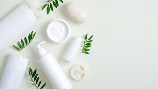 White body wash bottles and cream jar with green leaves on a pale background