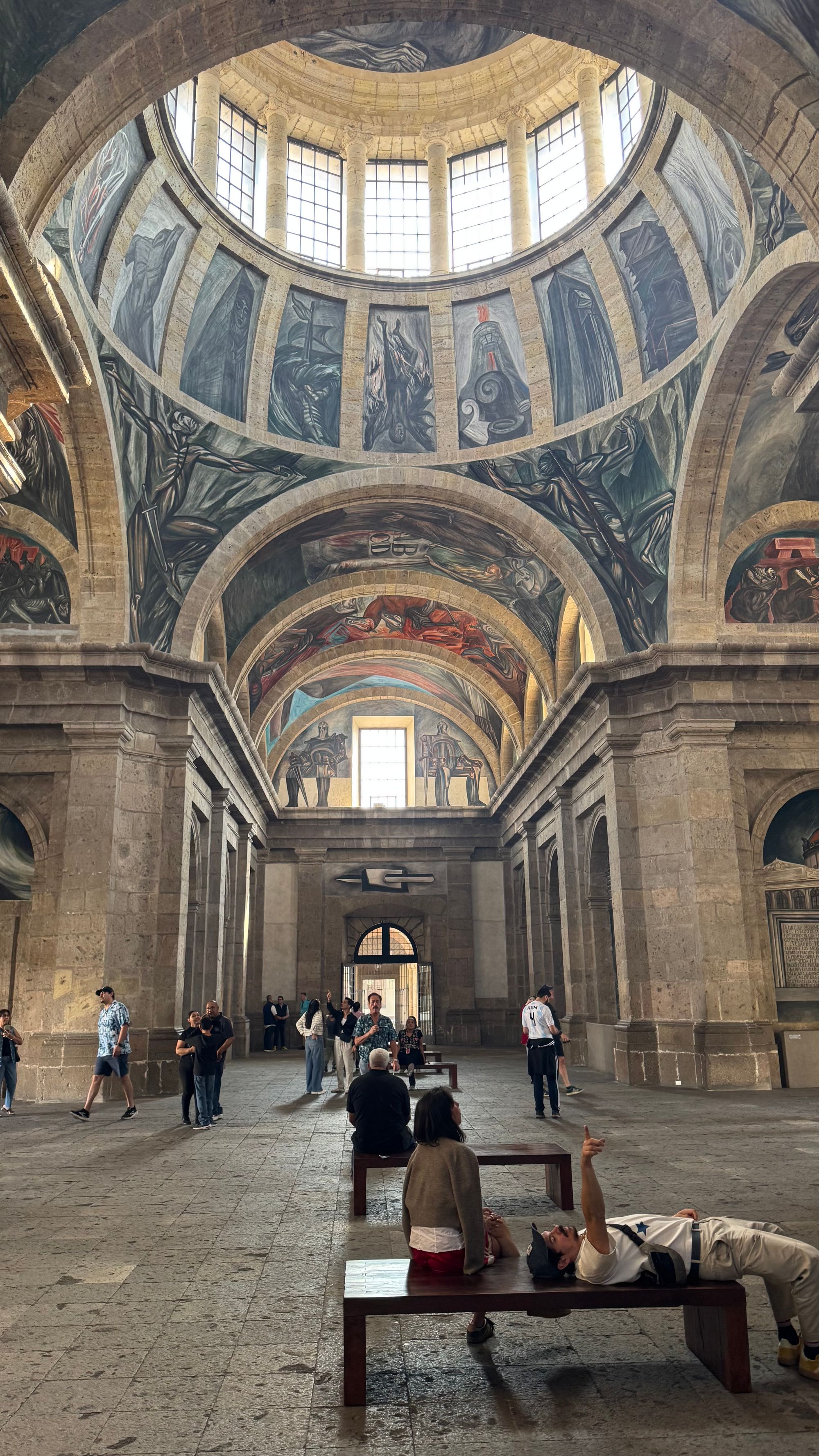 Museum goers lay on a bench to look at the painted ceiling