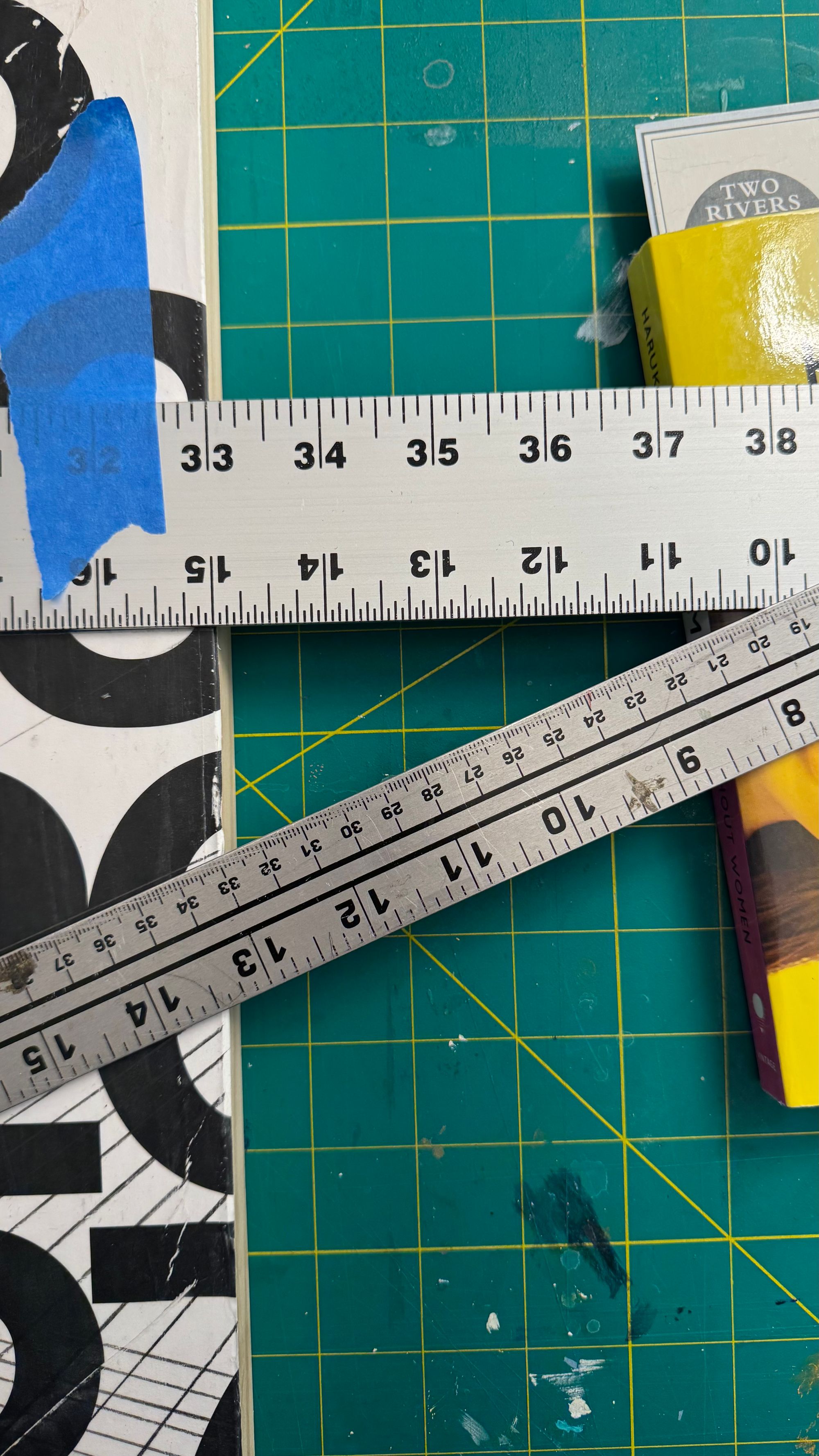 My work surface with two rulers taped to the surface of a painting, propped up by a short stack of books