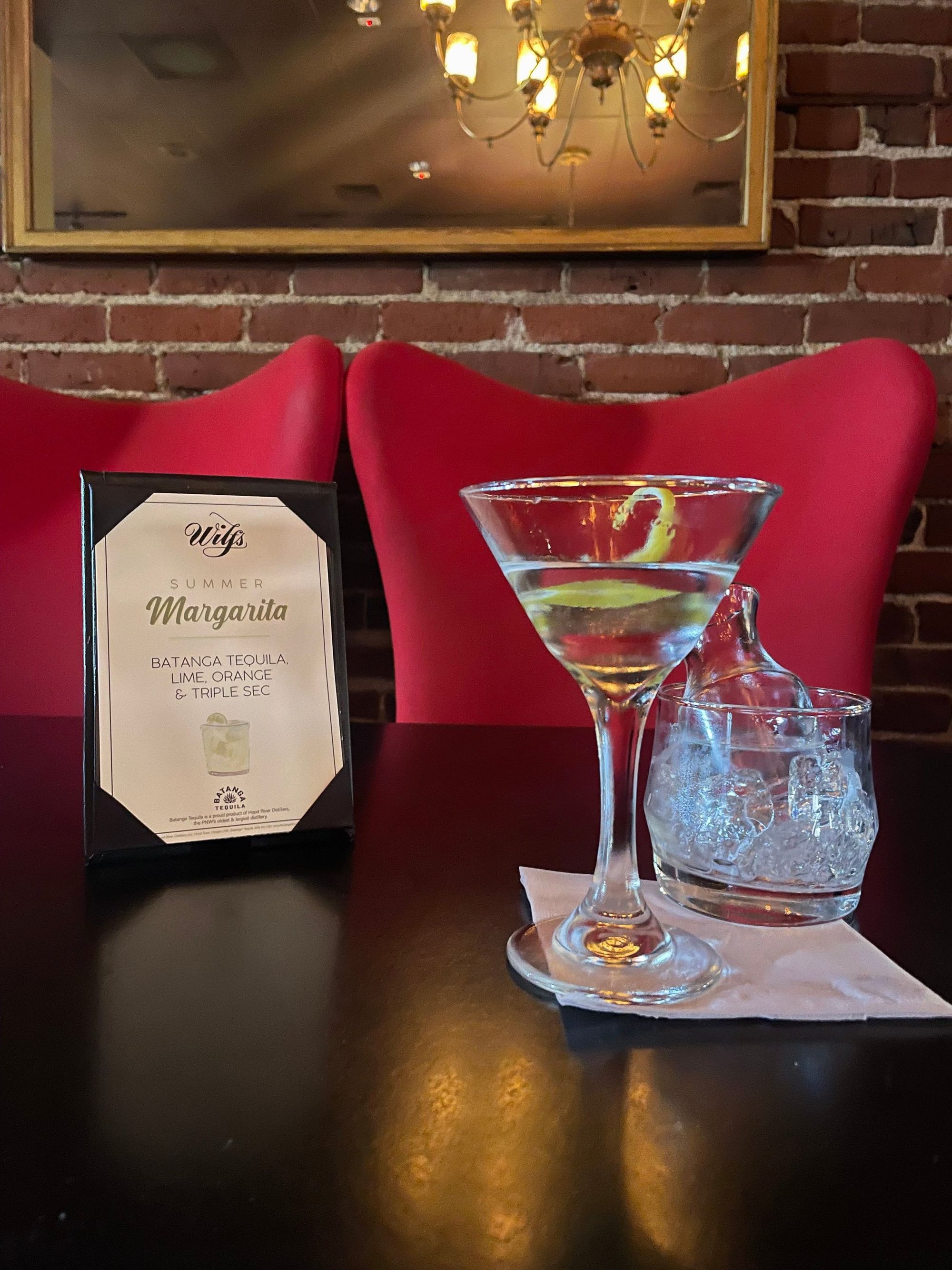 A martini in a cocktail glass sits on a table in front of red chairs.