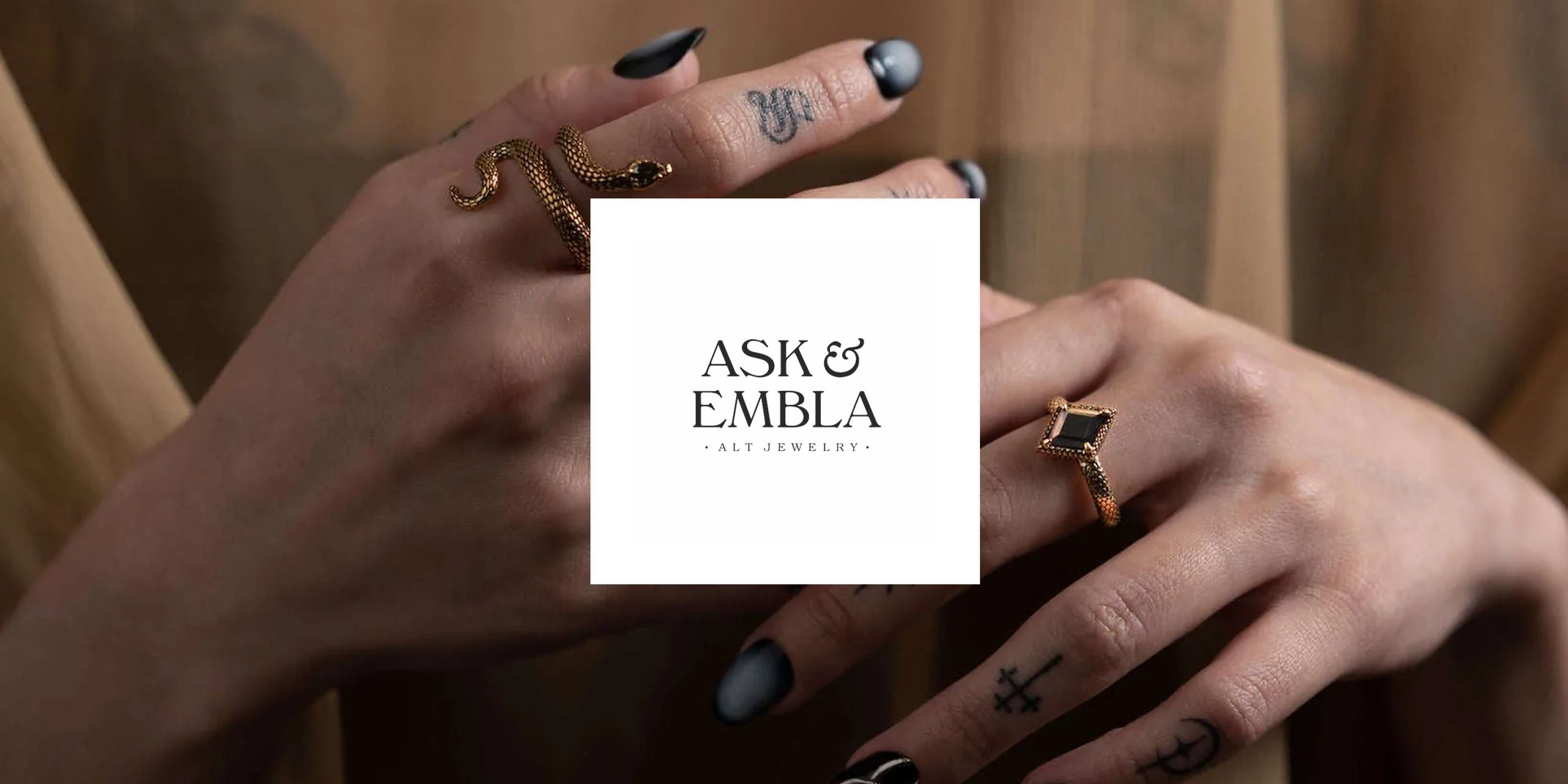 Hands wearing Ask & Embla rings around the Ask & Embla logo