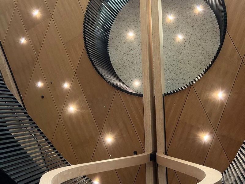 Diamond-jointed timber soffit with a circular opening ringed by dark battens, above a curved timber handrail