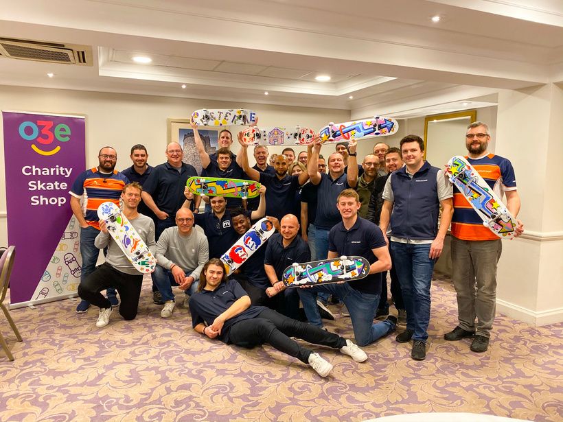 A team holding up the skateboards they decorated at an o3e charity skate shop event
