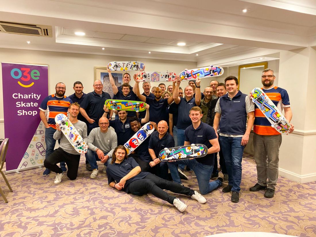 A team holding up the skateboards they decorated at an o3e charity skate shop event