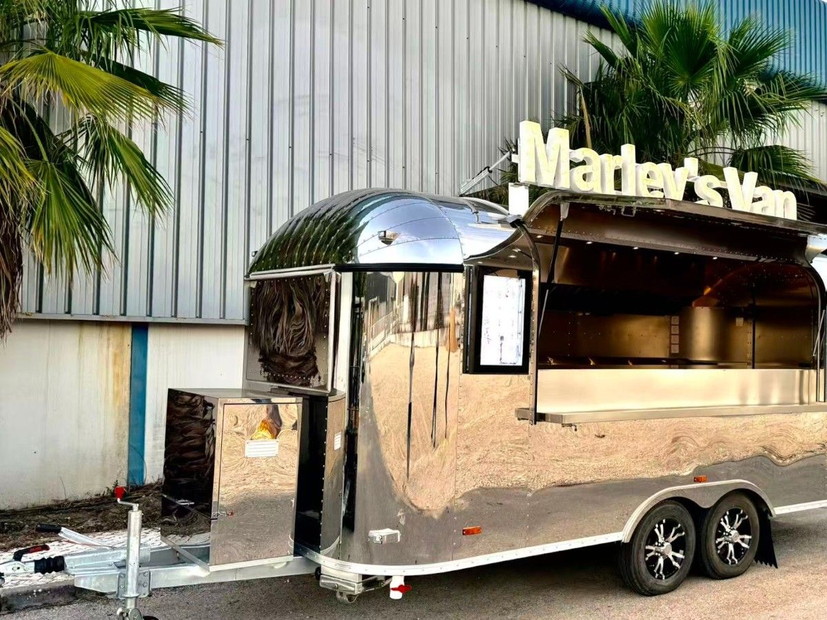 Shiny mirror polished Chris Machinery Airstream food truck setup outdoors under trees