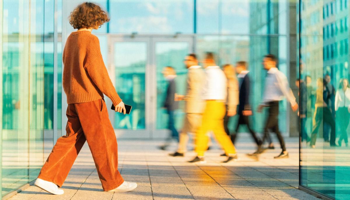 A single person mid-stride through a London tech atrium at golden hour, phone in hand — the moment before a commercial decision.