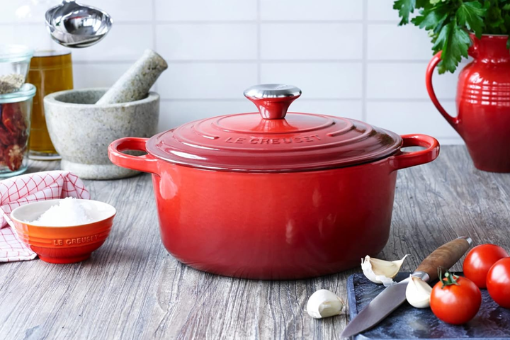A vibrant cherry-red Le Creuset enameled cast iron Dutch oven with a gleaming stainless steel knob on a clean stovetop.