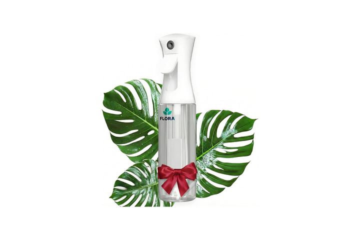 An elegant, vintage-style brass and tinted glass fine-mist plant spray bottle mister sitting infront of lush, sunlit green Monstera plants