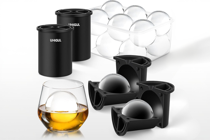 A large, crystal-clear spherical ice ball melting slowly inside a premium crystal lowball glass filled with an amber craft cocktail on a dark marble surface.