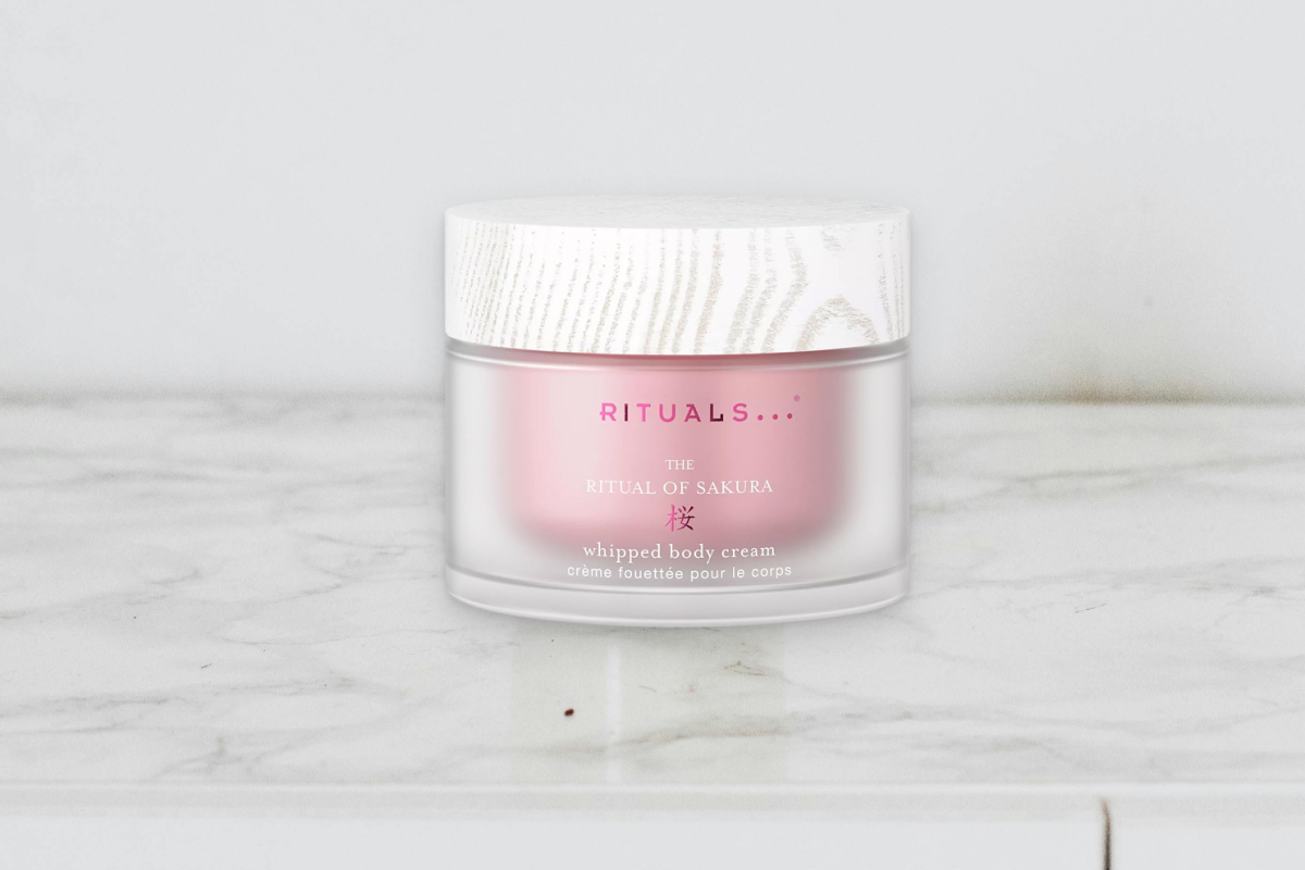 A luxury tub of Rituals The Ritual of Sakura body cream next to delicate pink cherry blossom petals.