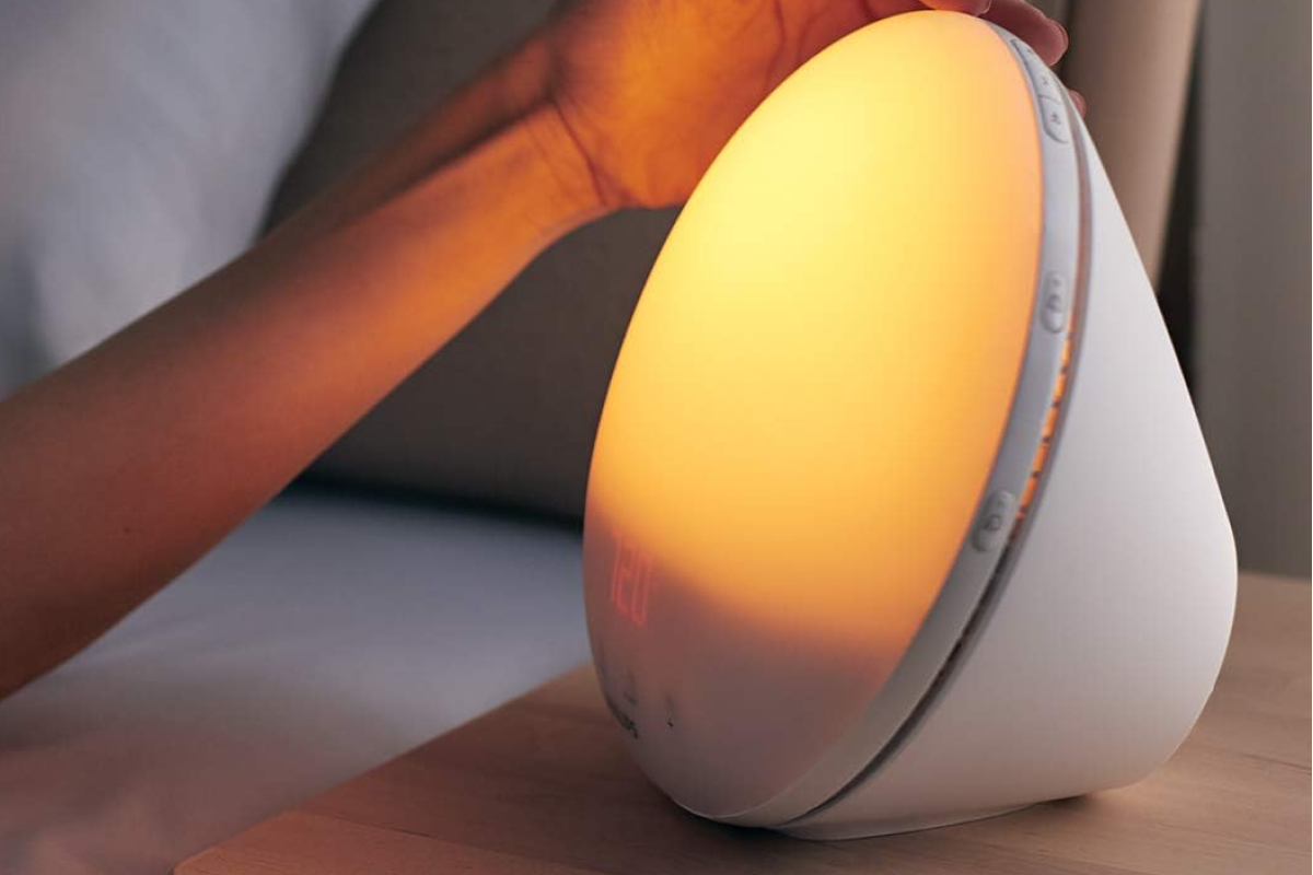 A Philips wake-up light sunrise alarm clock emitting a gentle, natural morning glow in a dark bedroom.