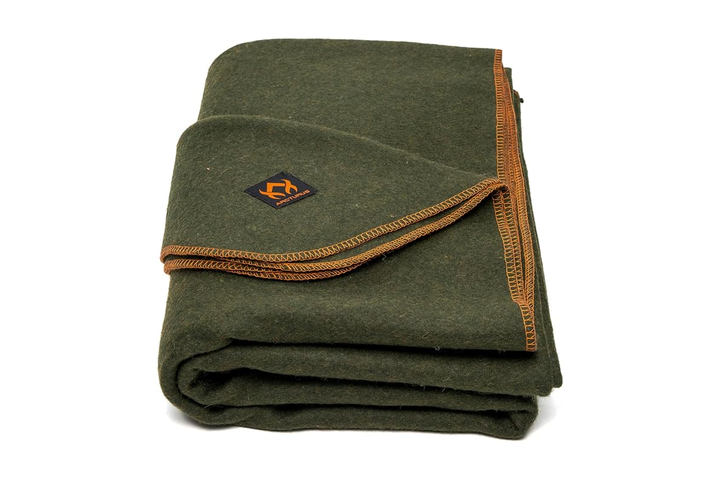A premium, charcoal-gray weather-resistant outdoor blanket with a plush fleece lining, neatly folded on a rustic wooden bench next to a glowing fire pit.