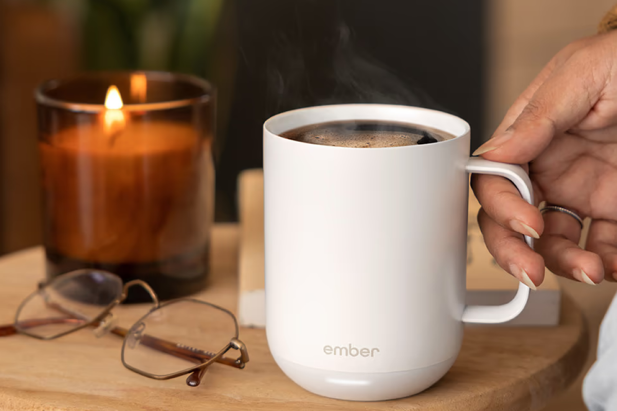 A sleek, matte white Ember temperature control smart mug sitting on its charging coaster with a soft glowing LED light.