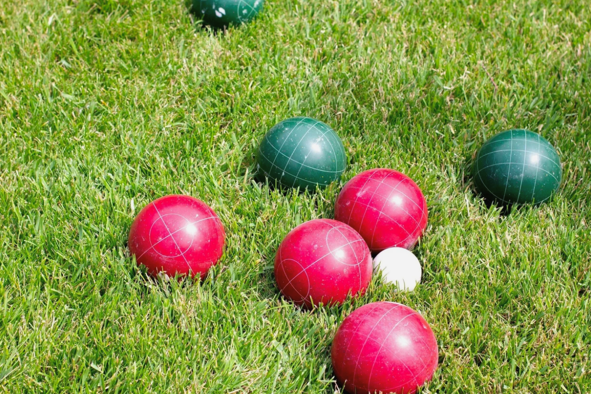 A high-quality wooden lawn game set up on green grass next to two glasses of crisp, cold rosé wine.