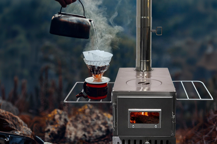 A compact, heavy-duty stainless steel portable wood burning stove radiating warmt as water is being porn onto a coffee drip filter