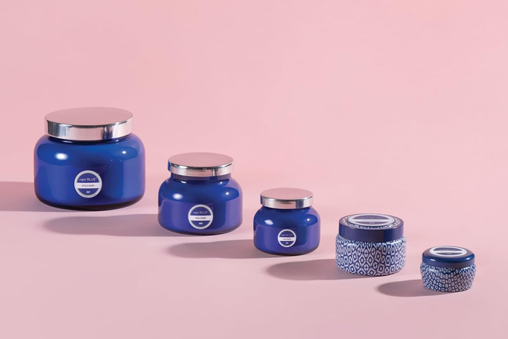 The iconic blue faceted glass jar of a Capri Blue Volcano candle lit and glowing warmly on a chic vanity table.