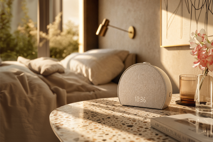 The Hatch Restore sleep machine glowing with a soft, warm sunrise light on a minimalist bedside table.