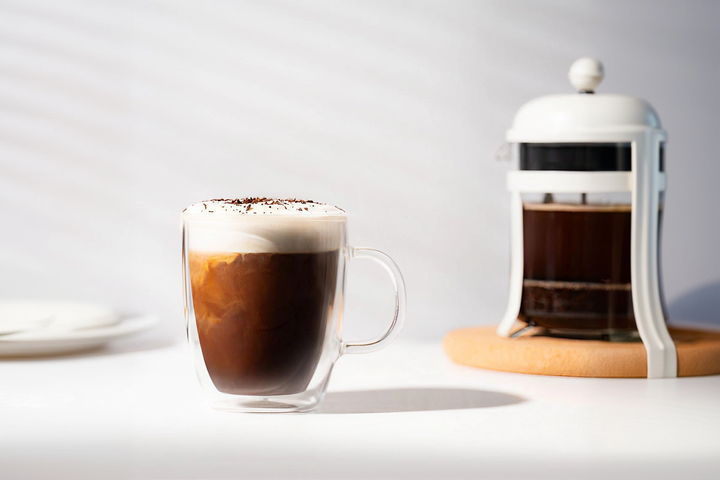 An elegant double-walled insulated glass coffee mugs filled with beautifully layered lattes and rich foam, resting on a minimalist marble table.