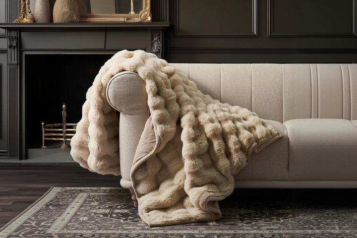 A close-up of a high-end, cream-colored ribbed faux fur luxury throw blanket elegantly draped over a plush modern sofa under warm, ambient living room lighting.
