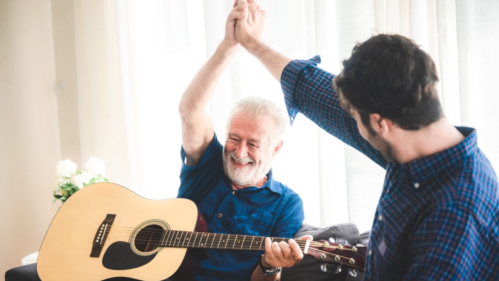 An adult hipster son and senior father at home, playing guitar and enjoy with music