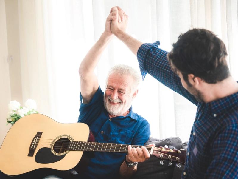 An adult hipster son and senior father at home, playing guitar and enjoy with music