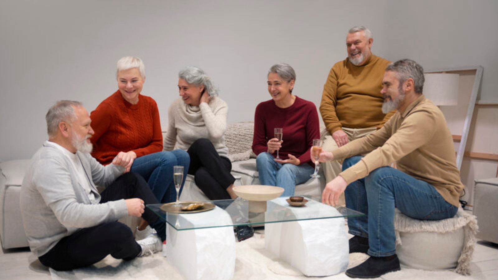 Group of smiling senior adults socializing together in a comfortable living room, enjoying conversation and refreshments in a welcoming board and care or assisted living community.