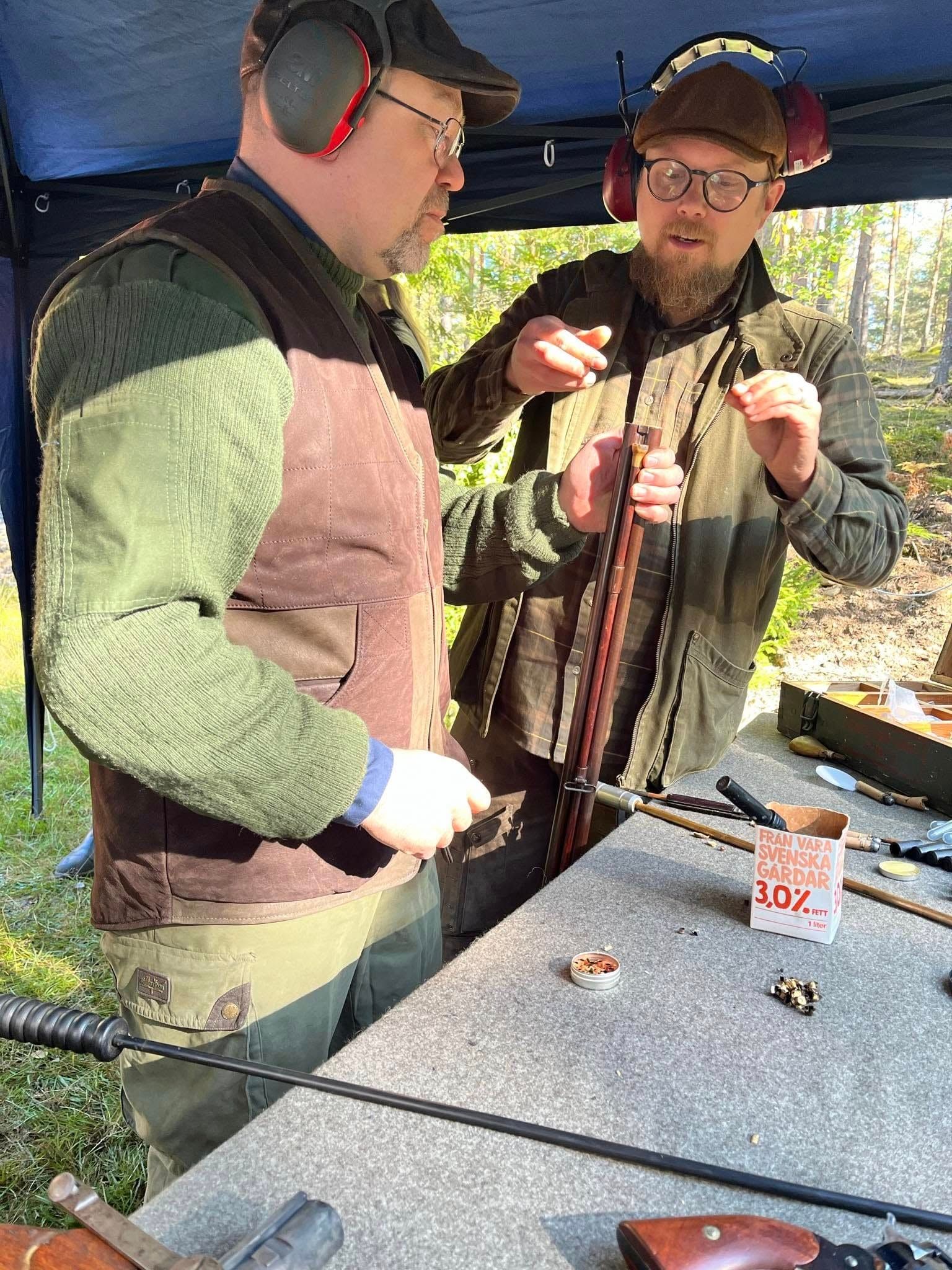 Urval av antika gevär, pistoler och revolvrar på ett bord utomhus.