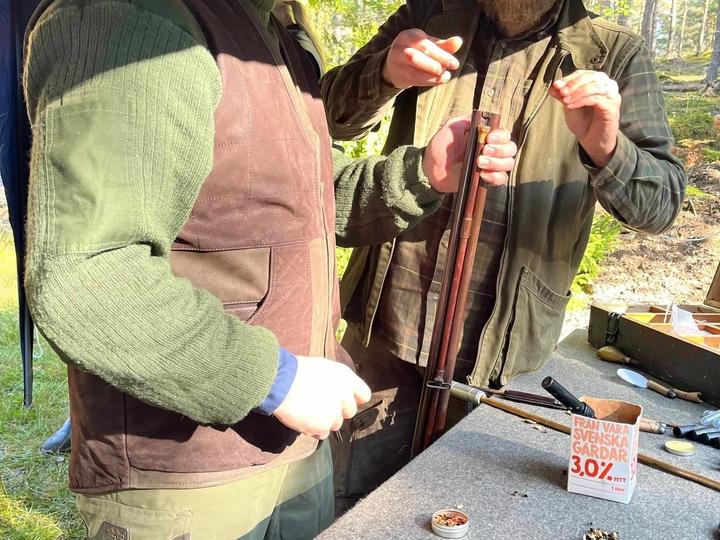 Urval av antika gevär, pistoler och revolvrar på ett bord utomhus.