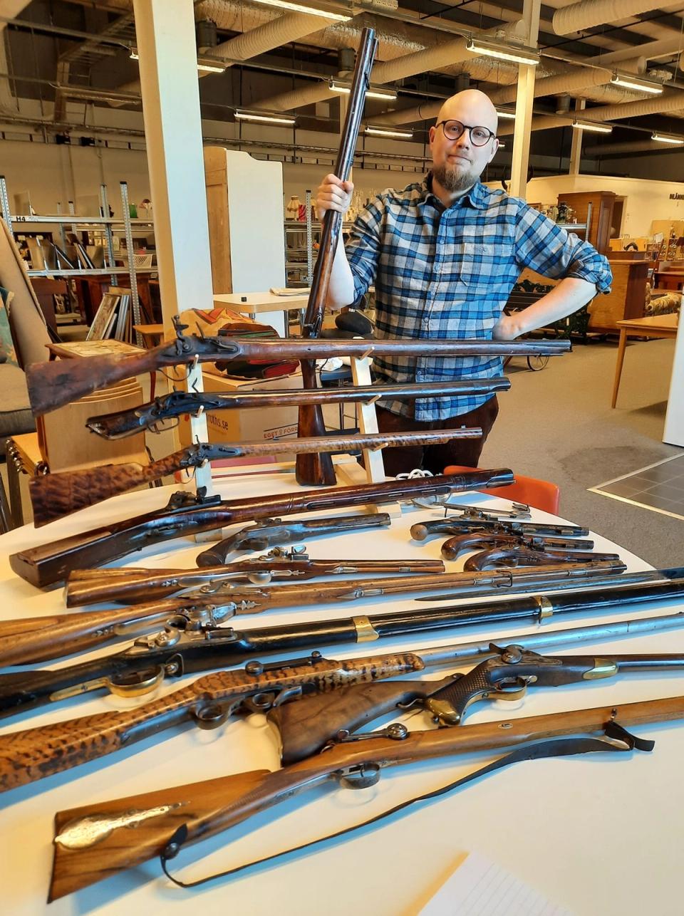 En man visar en samling antika vapen i en utställningsmiljö.